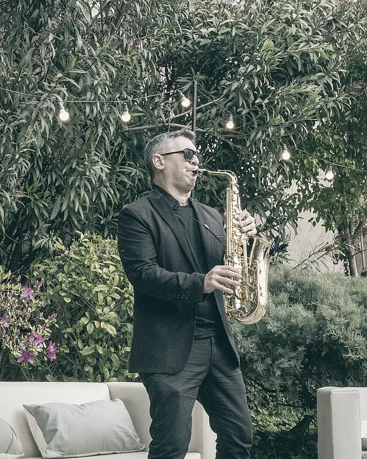 Saxofonista tocando en el jardín, entre luces cálidas