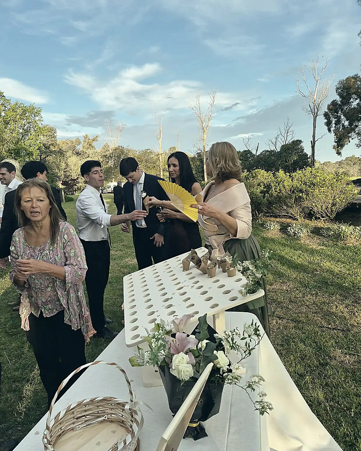 Invitados repartiendo conitos de pétalos y abanicos amarillos en el jardín