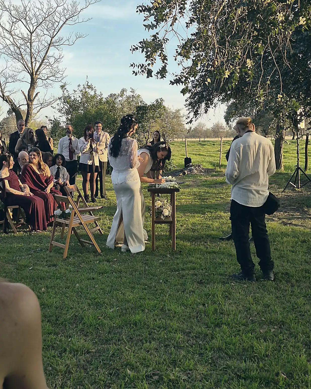 Una de las novias firma el acta sobre una mesa de madera con flores blancas