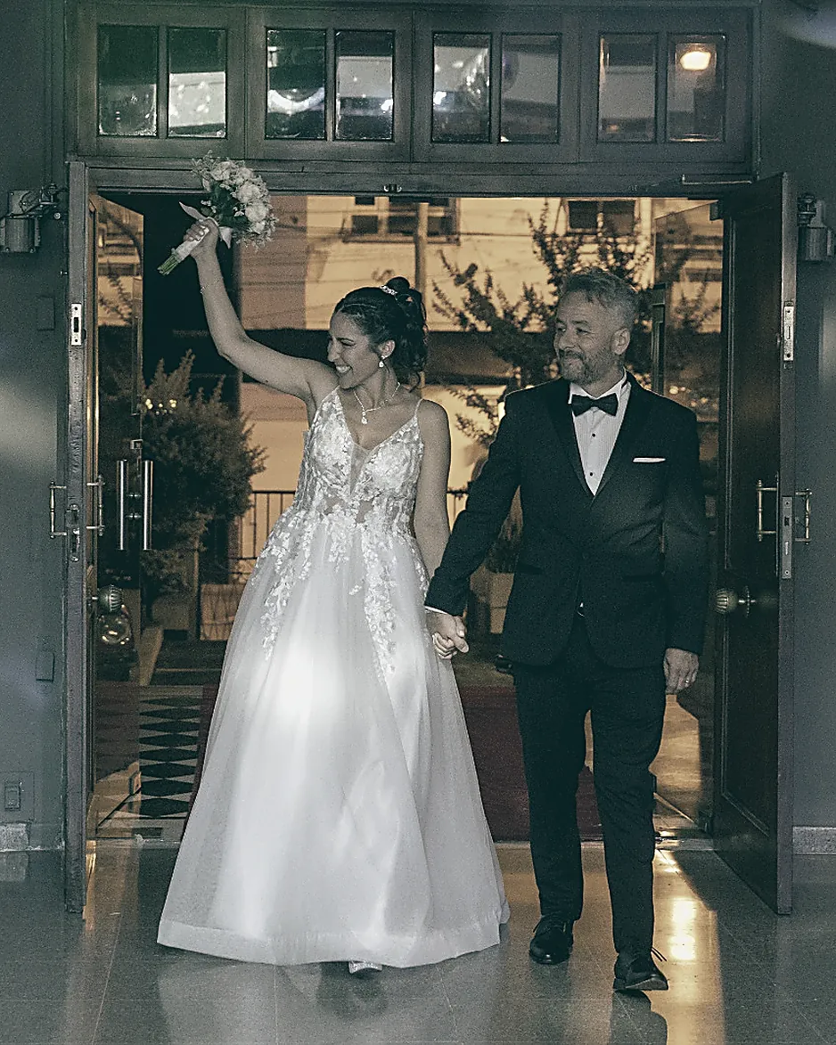 Los novios saliendo tomados de la mano, ella con el ramo en alto
